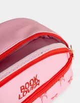 Cartuchera rosa con estampado de moños rojos, cierre superior con tirador dorado y la inscripción "Book Lover" en rojo.
