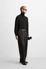 Pantalón negro de corte recto con cinturón de cuero sintético, pliegues frontales, bolsillos laterales y traseros con solapa.