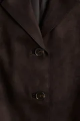 Campera tipo blazer o chaqueta de tejido suave con acabado cepillado, color marrón oscuro. Presenta solapas de muesca, cierre frontal de tres botones y dos bolsillos parche grandes en la parte delantera inferior.