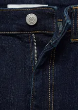 Pantalón de jean azul oscuro, de tiro medio, corte ajustado en la cadera y muslos, y acampanado desde la rodilla. Tiene cinco bolsillos, cierre frontal con cremallera y botón, y trabillas para cinturón.