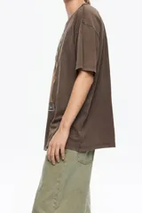 Camiseta de algodón orgánico color beige, corte oversize y manga corta ancha. Presenta un estampado central enmarcado con motivos florales y el texto "BIMBA Y LOLA" en la parte superior e inferior del diseño.