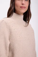 Sweater de punto color crudo, con cuello alto, manga larga y diseño holgado. Presenta un patrón de punto acanalado vertical y un diseño en forma de 'V' con pequeños agujeros decorativos en el pecho y los antebrazos.