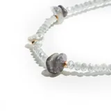 Pulsera de cuentas facetadas color celeste, con detalles de perlas, piedras grises irregulares y herrajes dorados.