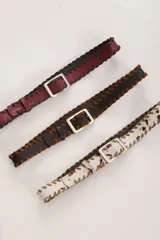 Cinturón de cuero color bordó con costura de tientos en color azul oscuro a lo largo de los bordes. Posee hebilla metálica rectangular plateada.