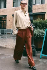 Pantalón marrón de tiro alto con bolsillos delanteros y falsos bolsillos traseros con tapeta. Detalle de pliegues en la parte delantera. Cierre frontal con cremallera y gancho metálico.