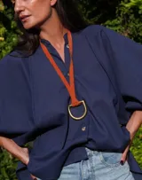 Collar con tira de cuero color suela y dije metálico dorado en forma de estribo.