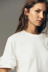 Camiseta negra de algodón con cuello redondo, manga corta y detalle de flores con volumen en las mangas.