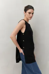 Blusa sin mangas negra de punto suave y fluido, con silueta larga y recta. Presenta botones dorados en los laterales.