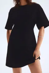 Vestido corto negro de punto de algodón suave con cuello redondo ribeteado acanalado, hombros caídos y mangas al codo. Pinzas moldeadoras en la parte posterior de la cintura para estilizar la figura.