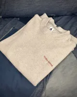 Buzo color gris claro tejido en punto Nantes, de corte holgado y mangas largas. Presenta un pequeño bordado con el logo de la marca en el pecho.