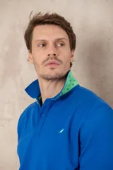 Chomba azul con cuello clásico, tapeta de dos botones y logo bordado en el pecho.