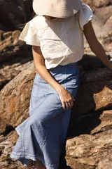 Falda larga de algodón color azul claro, con paneles verticales pespunteados en hilo blanco que estilizan la figura. La falda tiene una silueta amplia y fluida.