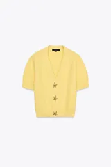Chaqueta amarilla de punto con escote de pico y manga corta. Cierre frontal con botones en forma de estrella.