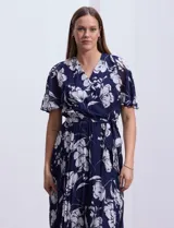 Vestido largo de gasa estampada con flores blancas sobre fondo azul marino, marca Sandra Darren. Tiene escote en V cruzado, cintura elastizada con lazo de ajuste, falda plisada y forro interno a tono.