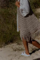 Bolso grande tejido a crochet con trapillo color marrón, con flecos en la parte inferior y etiqueta de cuero con el logo de la marca.