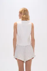 Chaleco negro sin mangas con escote en V y cierre cruzado con hebilla metálica.