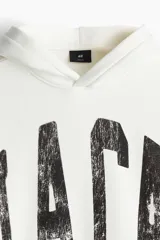 Canguro blanco con capucha forrada cruzada, bolsillo canguro y diseño estampado con letras negras. Corte holgado con hombros caídos y remate acanalado en puños y bajo.