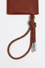 Monedero negro de piel con estructura blanda, asa de mano de cordón extraíble, logo metálico, acabados metálicos plateados, bolsillo interior y cierre con cremallera. Interior con etiqueta de tejido BIMBA Y LOLA.