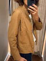 Chaqueta color caramelo de lino y algodón, con cuello mao, cierre frontal con botones de madera, bolsillos de parche y pespuntes a contraste.