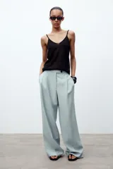 Pantalón de tiro medio color celeste confeccionado en hilatura con mezcla de lyocell. Tiene bolsillos laterales, pinzas delanteras, pierna ancha y cierre frontal con cremallera y botón.