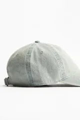 Gorra de denim celeste con ojales bordados en la parte superior, trabilla ajustable con hebilla de metal en la parte trasera y cinta antitranspirante de algodón.