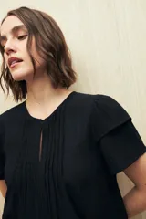 Blusa blanca de tela liviana con mangas cortas con volados y botón de nácar.