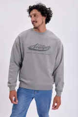 Buzo de algodón gris claro, corte oversize, con cuello redondo y puños y ruedo acanalados. Estampado frontal con el logo de "The Avengers" y el texto "Team up. Save the world. Repeat.".