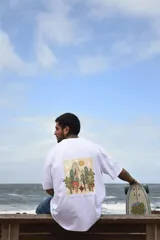 Remera blanca de algodón con estampado en la espalda de un paisaje con árboles, montañas y el sol.