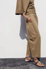Pantalón color marrón claro, de tiro medio, corte ancho y largo tobillero. Cuenta con cintura elástica ajustable con cordones y bolsillos laterales ocultos en la costura.