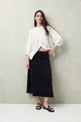 Falda midi de denim negro con tiro bajo, corte evasé, costuras verticales y ruedo desflecado.