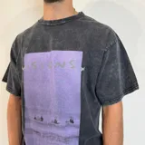 Remera negra con efecto lavado y estampado rectangular con imagen de surfistas en la playa y texto "Visions" en color lila. Corte oversize.