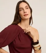 Vestido midi evasê color borgoña, confeccionado en viscolino, con escote asimétrico de un solo hombro, manga corta abullonada y frunces.