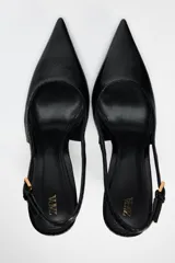 Zapato de tacón fino color negro con efecto relieve en el cuerpo, tira trasera con hebilla ajustable y acabado en punta.