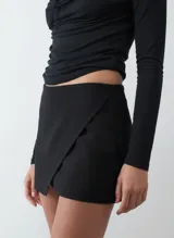 Short pollera negro de tiro medio, con diseño envolvente cruzado en el frente.
