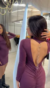 Vestido corto violeta de lycra, con cuello alto, espalda descubierta y detalle de cadena plateada.