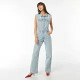 Mono largo de jean celeste, sin mangas, con cuello camisero, cierre frontal con botones, bolsillos delanteros y traseros, y cinturón con hebilla metálica.