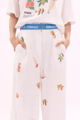 Pantalón blanco de corte amplio con estampado de motivos marinos y cintura elástica con cinturón azul con la inscripción 'Verano Mirando al Mar'.