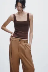 Pantalón de vestir color marrón claro, de tiro medio, corte ancho y con pliegues frontales.