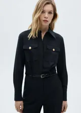 Mono largo negro de corte slim fit, con cuello camisero, cierre frontal con botones, cinturón con hebilla dorada, dos bolsillos de parche con solapa en el pecho, puños abotonados y trabillas.