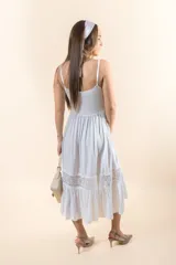 Vestido midi blanco de corte princesa, con breteles finos, escote en V, botones frontales, plisados en el torso y bordados de encaje en cintura y ruedo.