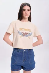 Remera color crema de corte cropped, con mangas cortas y estampa frontal con la frase "Rock and Roll" y un rayo alado. 