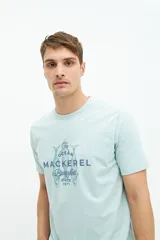 Remera verde agua de manga corta con estampado de dos peces y texto en azul marino.