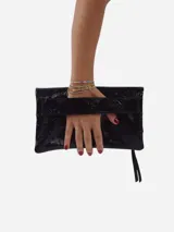 Sobre de fiesta negro charolado con cierre de solapa imantada y tira de cuero para sujetar a la muñeca.