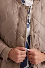 Campera larga acolchada color visón, con cuello redondo, cierre frontal con botones a presión y bolsillos laterales con cierre.