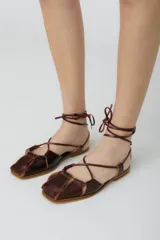 Sandalias chatitas de cuero color bordó, con puntera cuadrada y tiras finas que se atan al tobillo.