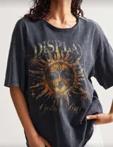 Remera marrón con cuello redondo y mangas cortas, con estampado de un sol con rostro en tonos ocre y azul. Corte holgado y estilo vintage.