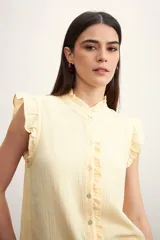 Camisa color amarillo pálido con cuello mao, sin mangas, con volados en los hombros y en el frente.