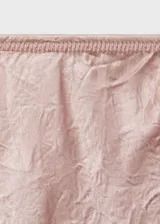 Falda midi de tiro medio, corte recto, color rosa pálido con efecto arrugado y brillo satinado. Presenta un diseño asimétrico en la parte superior, posiblemente superpuesto a un top blanco.