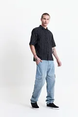 Camisa de manga corta con corte oversize, a rayas verticales blancas y grises, con cuello clásico y cierre frontal con botones. Confeccionada en algodón.