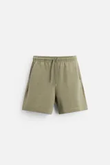 Bermuda color verde oliva de corte relaxed fit, confeccionada en tejido interlock de algodón con elasticidad. Tiene cintura elástica ajustable con cordón, bolsillos laterales y bolsillo trasero de plastrón.